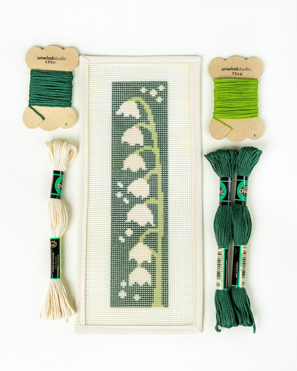 Needlepoint kit with a pattern of white flowers on a green background, surrounded by green and beige thread skeins.