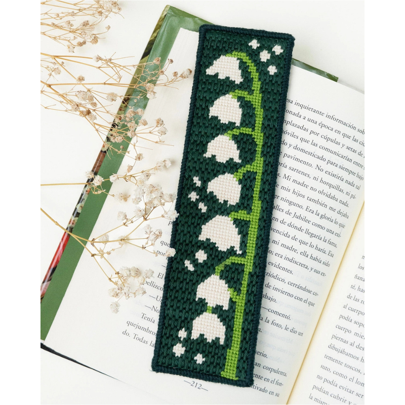 A needlepoint book bookmark with a green vine and white lily of the valley pattern, placed on open books with dried baby's breath flowers around it.