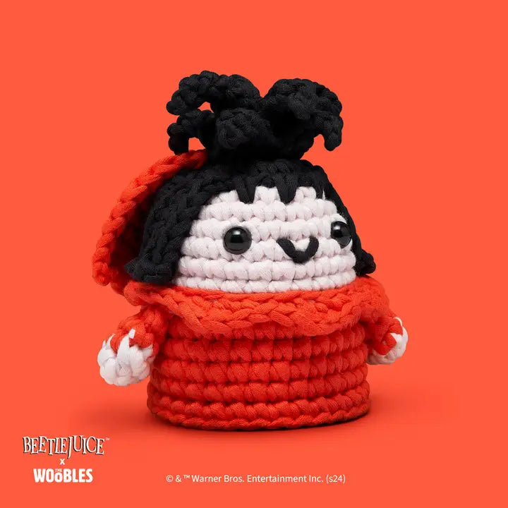 Crocheted character with red sweater and black hair on an orange background, featuring Beetlejuice branding.
