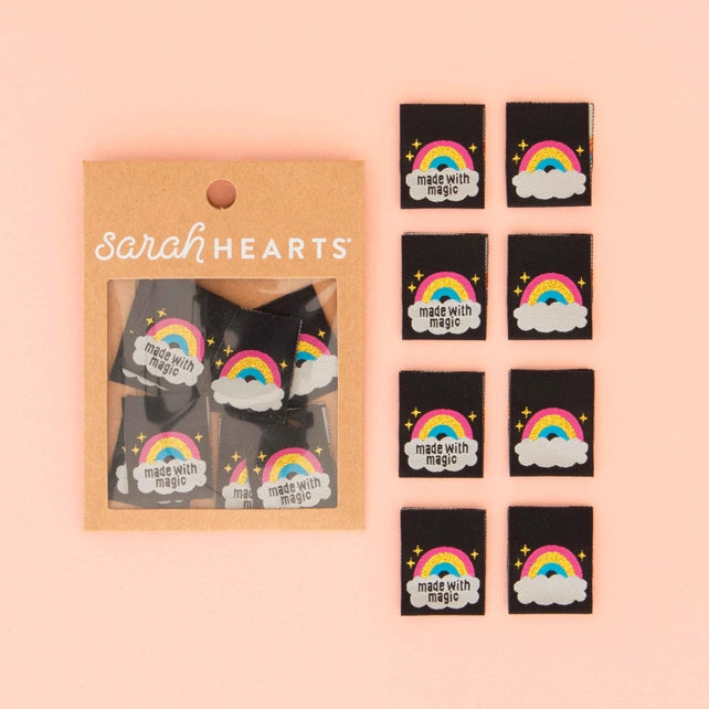 Packaged labels with rainbow and cloud designs labeled 'made with magic' by Sarah Hearts on a pink background.