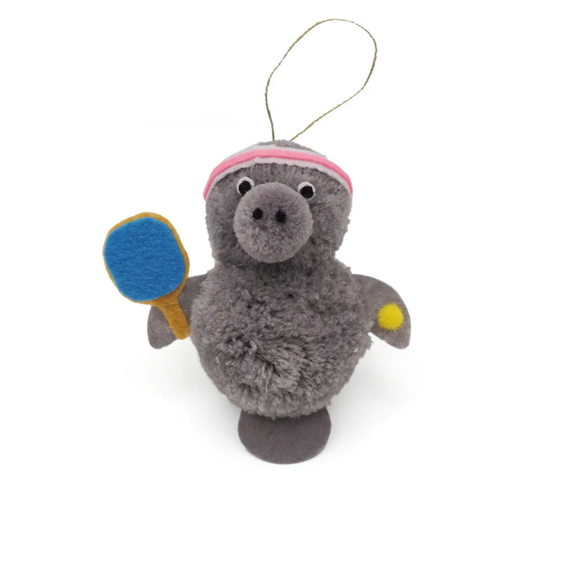 Gray manatee holding a ball and racquet pom pom ornament on a white background.