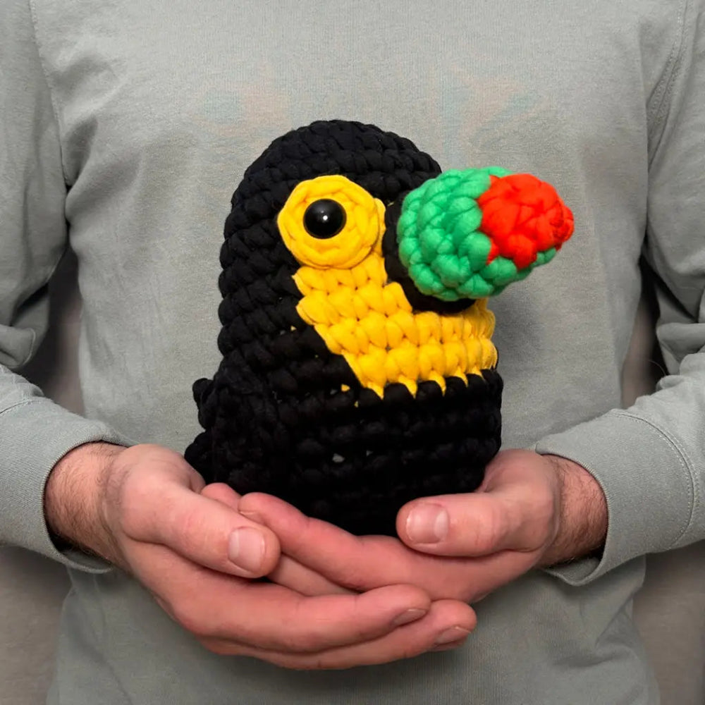 Handmade crocheted toucan toy held in hands against a grey long sleeve shirt
