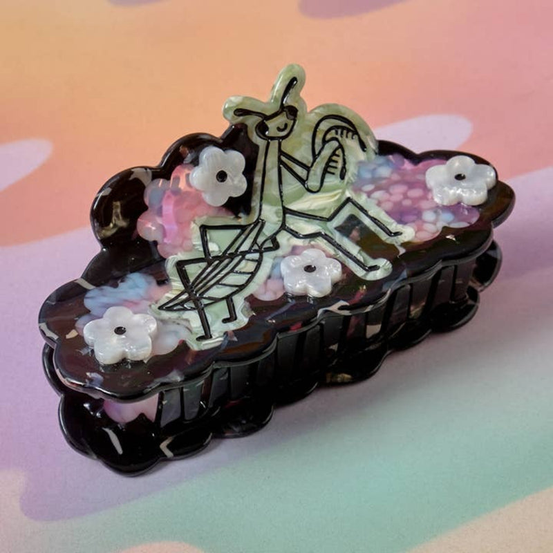 Decorative hair clip with mantis design and floral elements on a pastel background