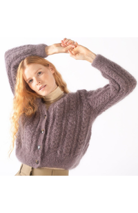 Red haired woman in a beige turtleneck, taupe pants, and a mauve fuzzy and textured knit cardigan on a white background