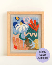 Framed needlepoint artwork with colorful abstract design on a white wall.