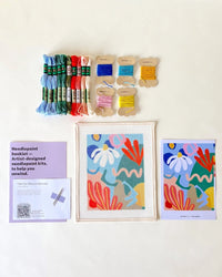 Needlepoint kit with thread, instructions, and canvas on a white background