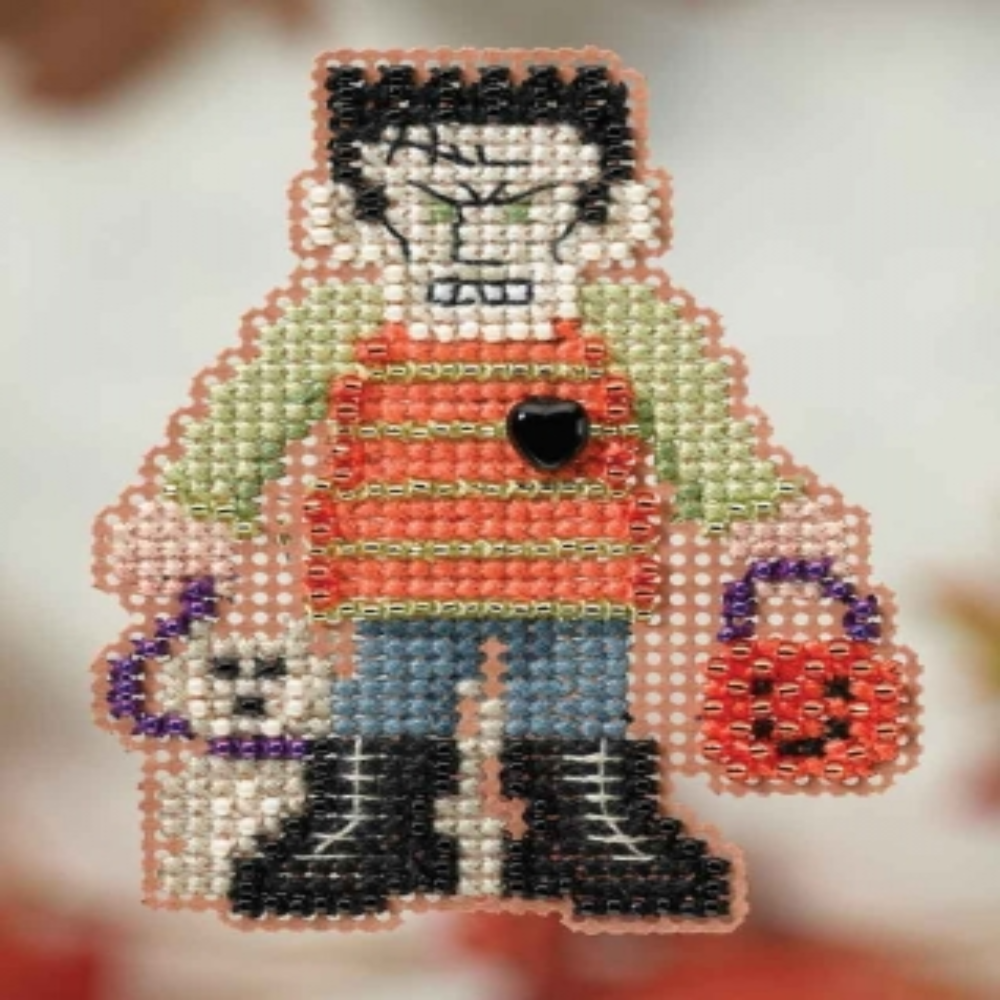 A beaded cross-stitch character featuring a stylized figure with black hair, a pale face, a red-orange striped top, blue pants, black boots, and trick or treat baskets, shown against a soft blurred light background.