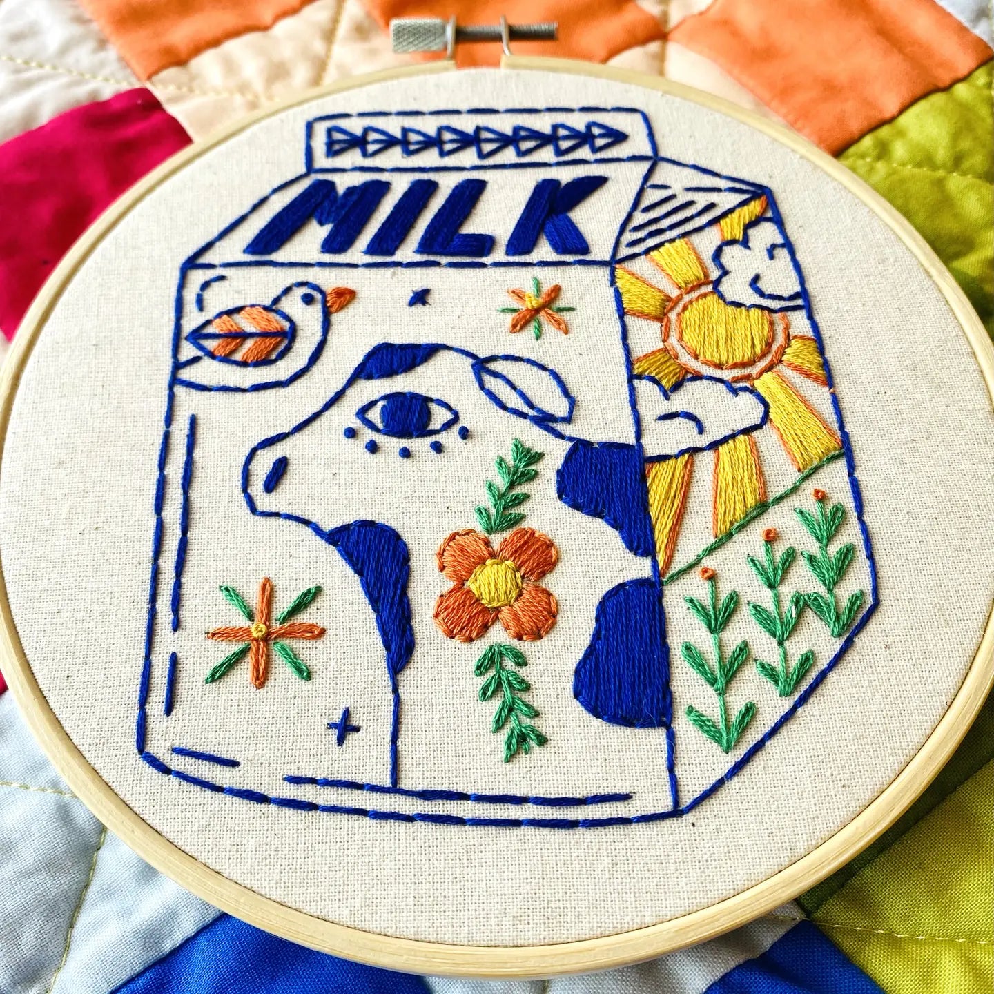 Embroidery hoop with a colorful milk carton design featuring flowers and plants.