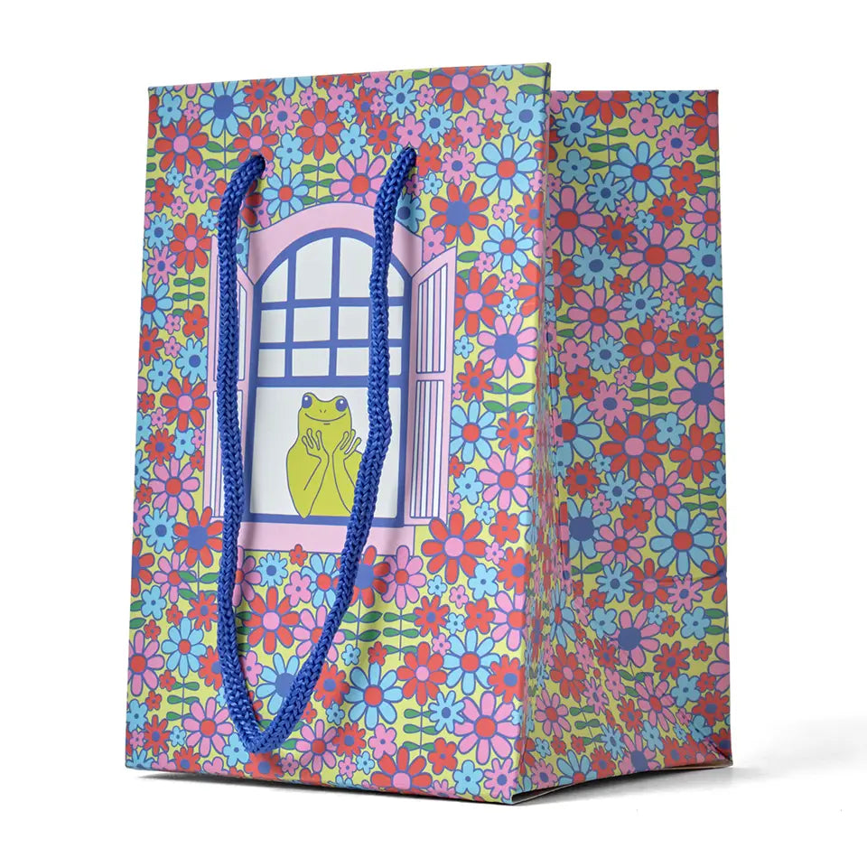 Gift bag with a design featuring a frog in a window and a floral background on a white background.