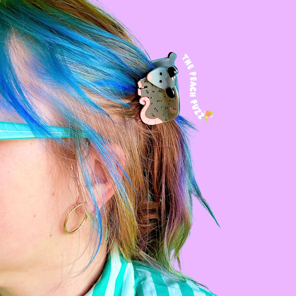 Person with colorful hair featuring a possum-themed hair clip against a pink background