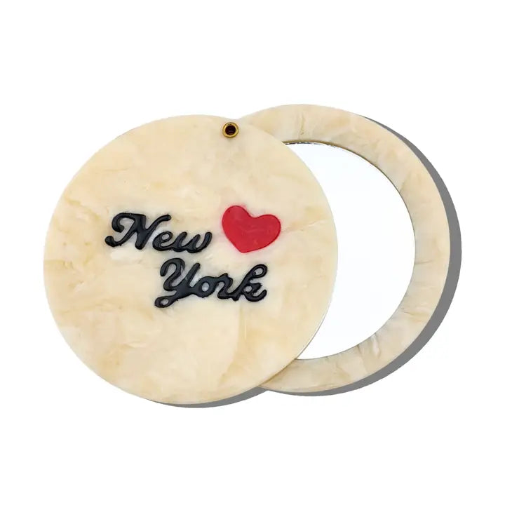 Circular off-white compact mirror with a red heart and black text reading "New York"