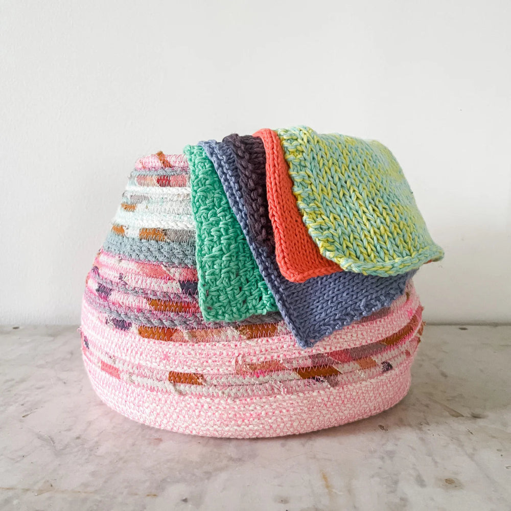 Colorful woven basket with folded knitted fabric swatches on a marble surface