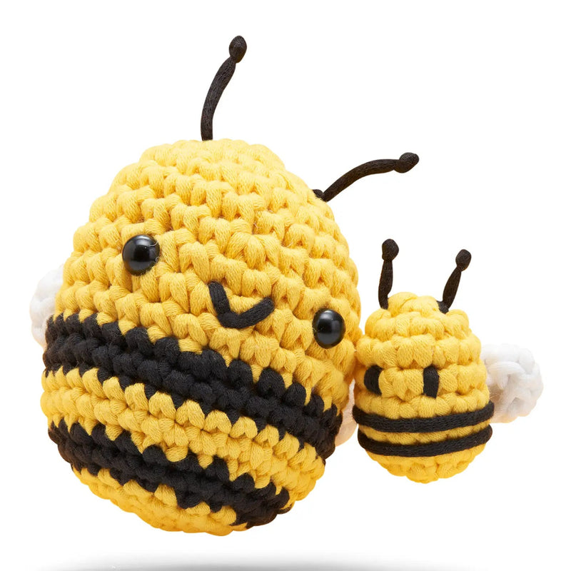 A yellow and black crocheted bee plush toy with white wings, shown next to a smaller matching bee on a clean white background.