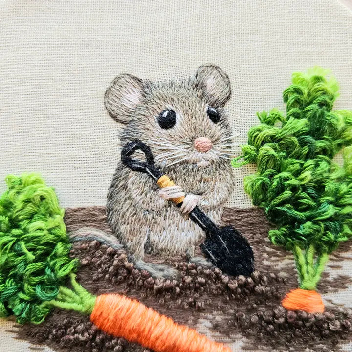 Closeup of embroidered mouse with a shovel digging up carrots