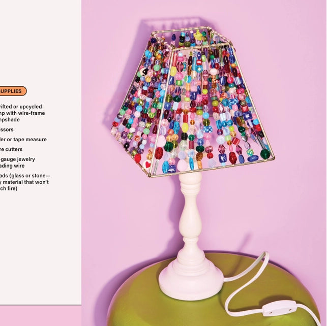 Beaded lampshade on a white base with colorful beads against a pink background