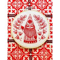 Embroidery hoop with red embroidered design of a gnome on a red and white patterned fabric background