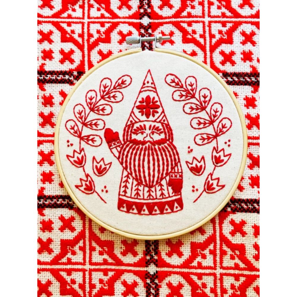 Embroidery hoop with red embroidered design of a gnome on a red and white patterned fabric background