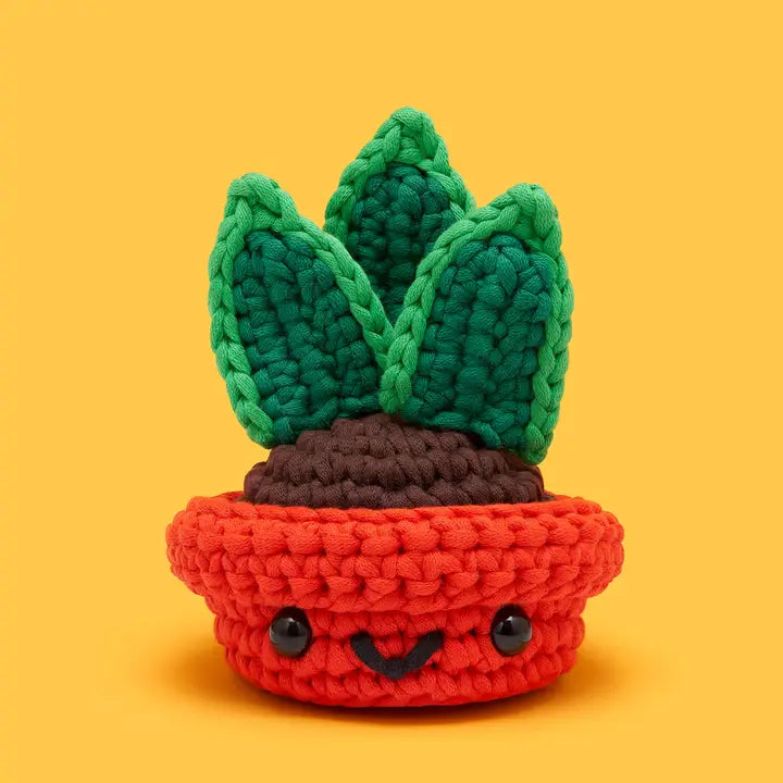 Crocheted potted plant with green leaves and a red pot on a yellow background