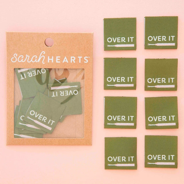 Green labels with 'OVER IT' text and a 'Sarah Hearts' packaging on a pink background