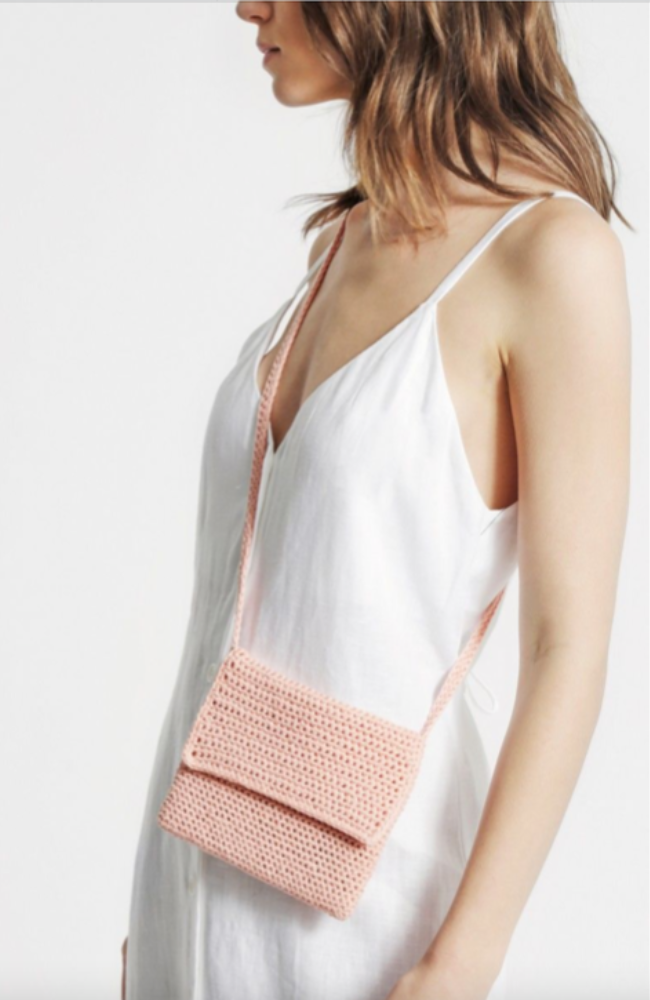 Model in a white dress with a crocheted pink crossbody bag.
