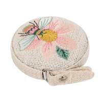 Round woven tape measure with embroidered bee and flower design on a white background