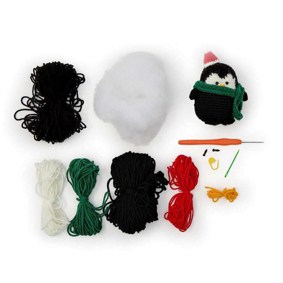 Crochet kit with yarn balls, a penguin figure, and crochet hooks on a white background