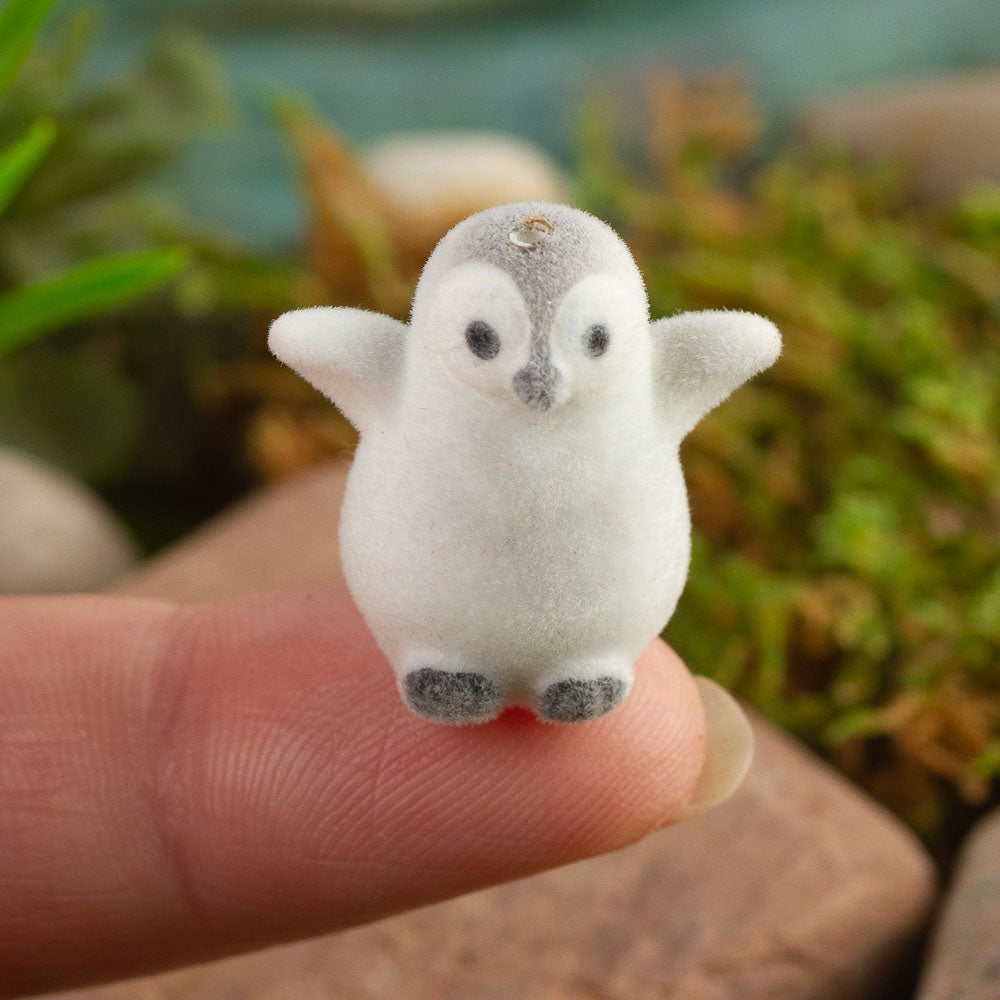 Small fuzzy penguin figurine held on a finger with a blurred natural background.