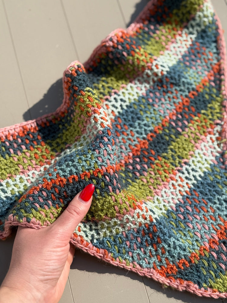 A hand with red nali polish holding the edge of a plaid crochet kerchief.
