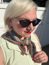 A woman with blode hair and sunglasses, wearing a plaid crochet kerchief tied at the  front of her neck.