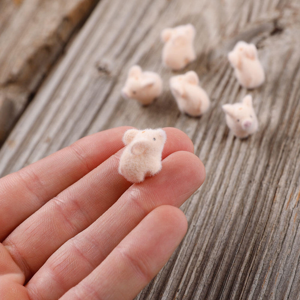 Small flocked pink pig held in a hand with more pigs on a wooden surface outdoors.