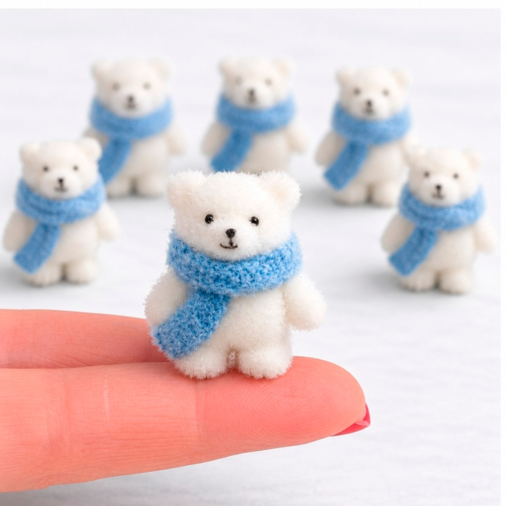 A small white polar bear fuzzy figurine wearing a blue knit scarf is displayed on a person's finger, with several similar bear figures blurred in the background.