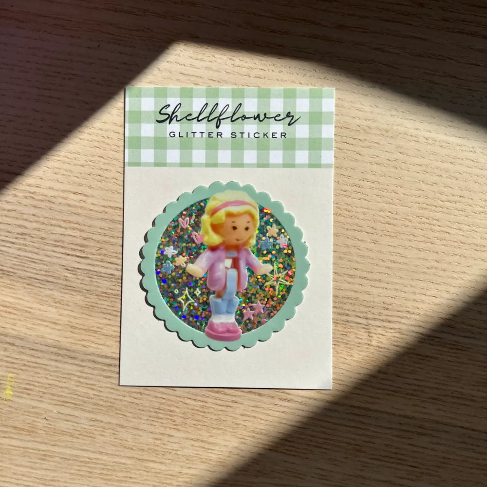 Glitter sticker with a character on a checkered label, placed on a wooden surface.