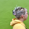 Person with a possum hair clip against a green wall