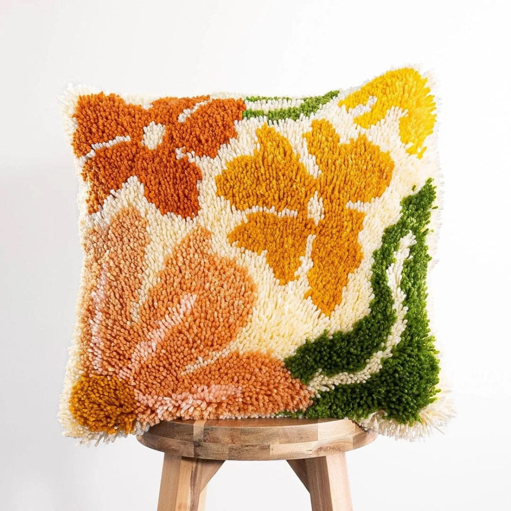 A fluffy pillow cushion featuring a mix of orange and pale peach flowers with green leaves on a pale beige background.
