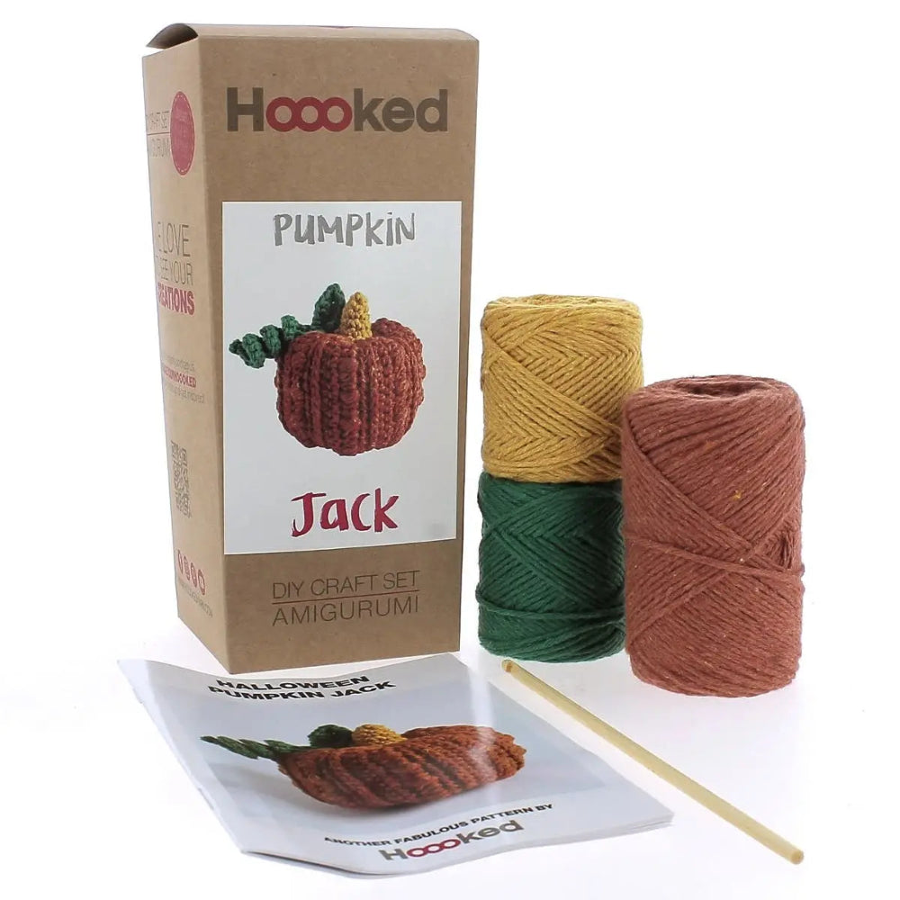The Pumpkin Jack crochet kit and all its contents: three colors of yarn, a crochet hook and an instruction booklet on a white background.