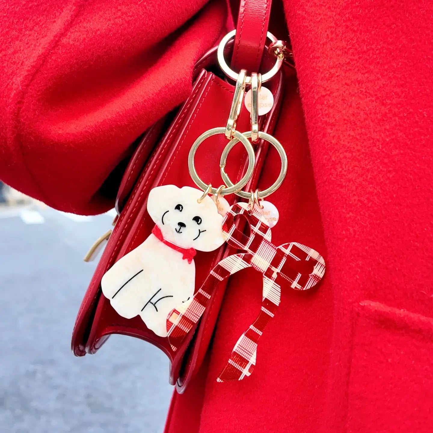 Keychains with a dog design and plaid bow design attached to a red bag.