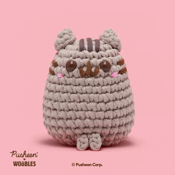 Plush toy resembling a cat with braided texture on a pink background, featuring the Pusheen brand.