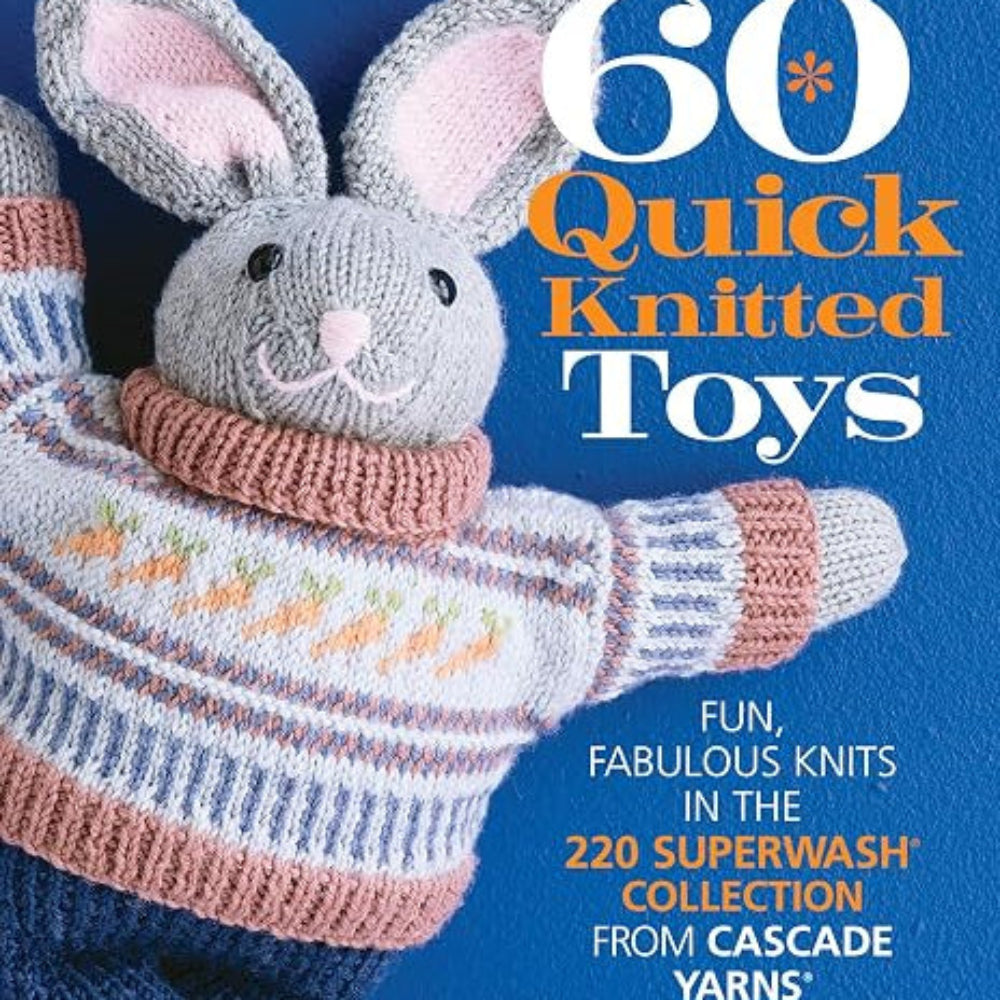 A grey plush bunny toy with a colorful knitted sweater with a carrot design and blue knitted jeans lays on top of a blue background. The text on the cover reads "60 Quick Knitted Toys: Fun, Fabulous Knits in the 220 Superwash Collection From Cascade Yarns" in white and orange text. 
