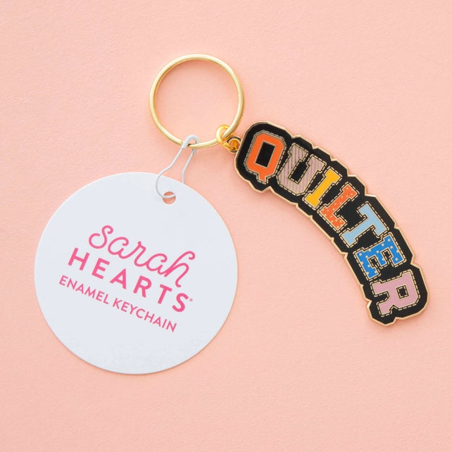 Colorful 'QUILTER' keychain with a round tag on a pink background