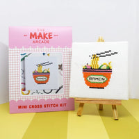 Make Arcade mini cross stitch kit with a completed cross-stitched design of a ramen bowl on a yellow surface.