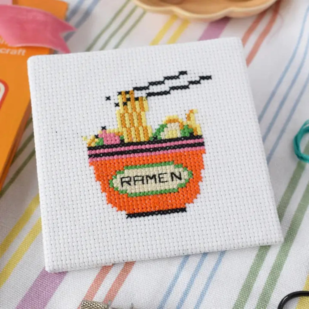 Cross-stitched design of a ramen bowl on white fabric.
