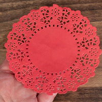 Red paper doily with intricate cut-out patterns held in a hand on a wooden surface