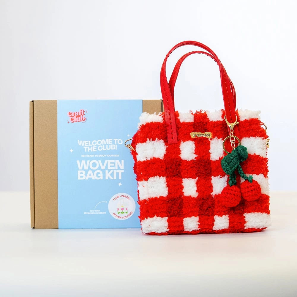 A fluffy red checkered purse with a cherry keychain rests against a box with the label "Woven Bag Kit".