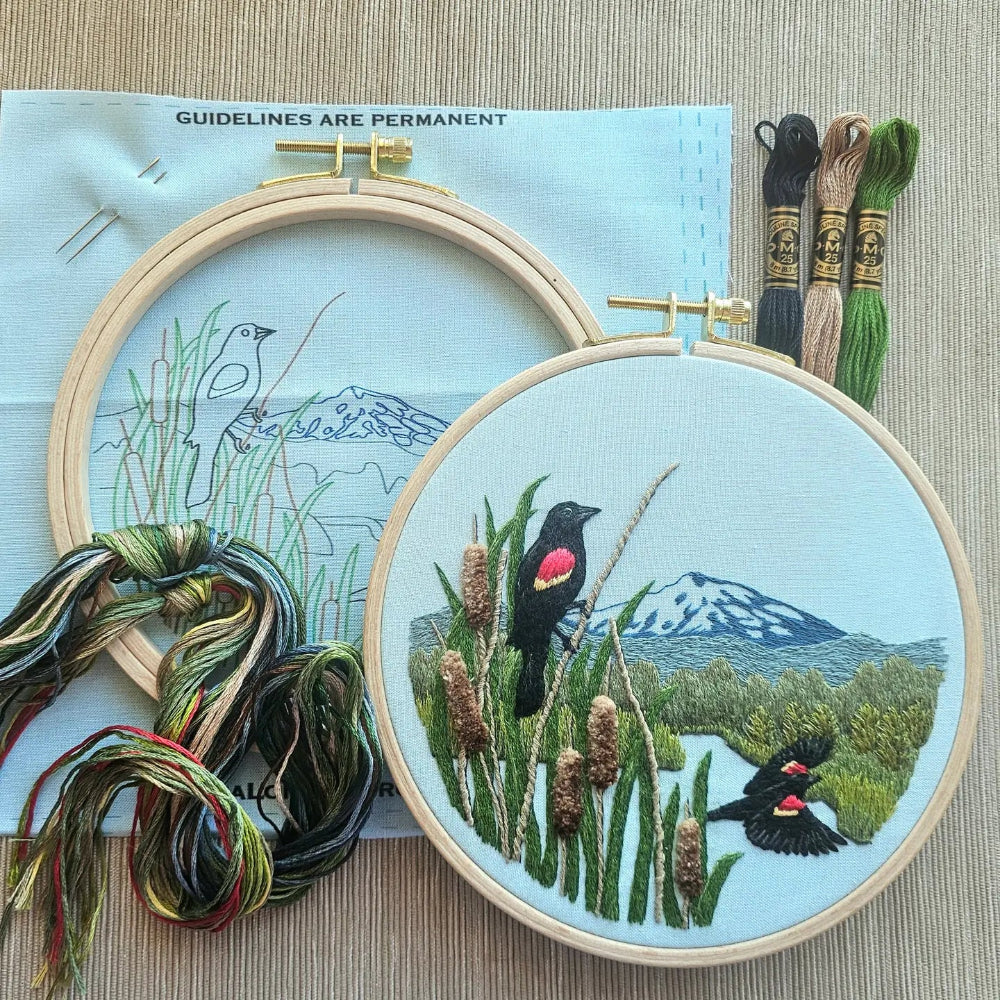 Embroidery hoops with embroidered red winged blackbirds and landscape on a textured surface. 
