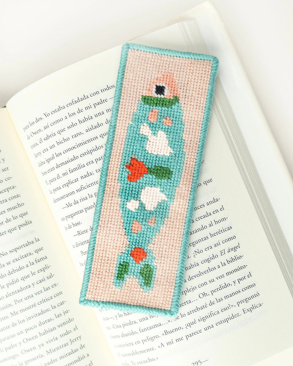 Needlepoint bookmark with a colorful fish design against an open book background