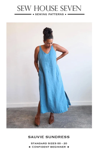 Model in brown shoes and light blue chambray tank dress on a white background and gray floor, framed in cream with Sew House Seven branding.