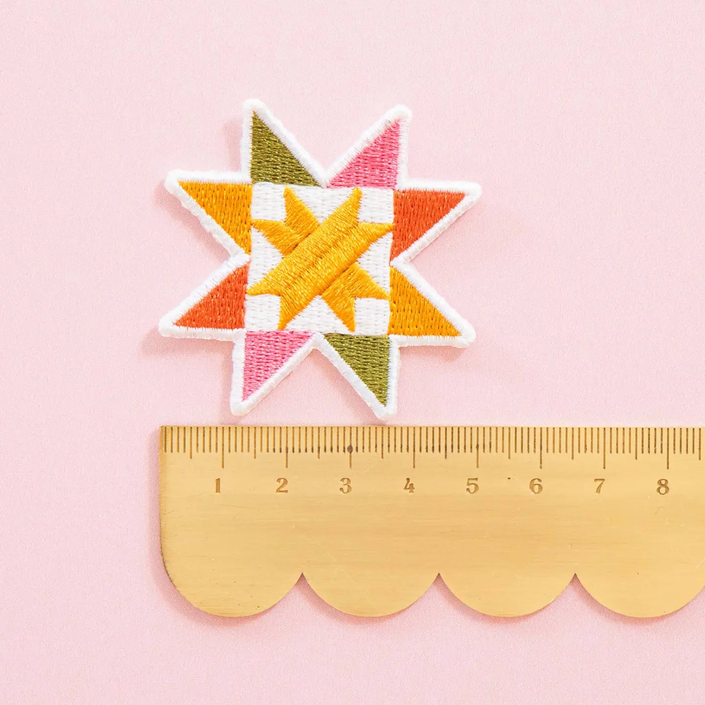 Colorful sawtooth quilt block patch on a pink background with a ruler for scale.