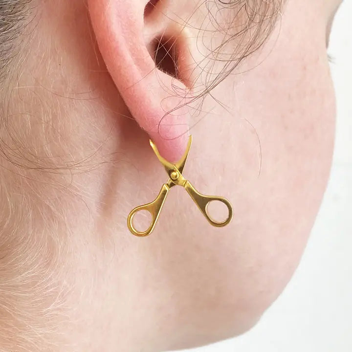Gold scissors earring worn on a person's ear