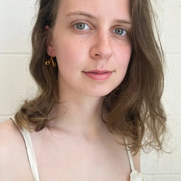 Woman with shoulder-length brown hair wearing a gold scissor earring against a white background