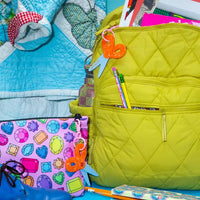 Scissors bag charm hanging on a green backpack